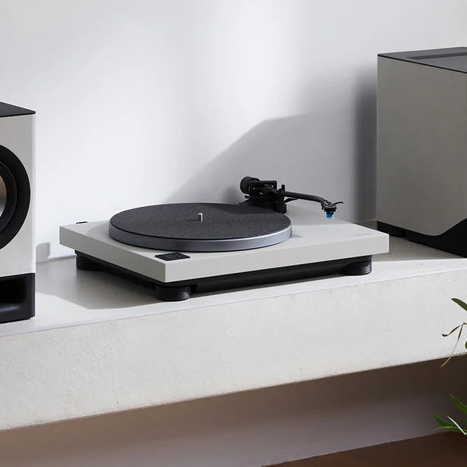 Audio equipment including speakers and a turntable on a white surface with a plant in the background.